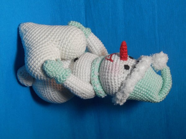 Weißer gehäkelter Amigurumi-Schneemann mit mintgrüner Mütze und Schal auf blauem Hintergrund.
