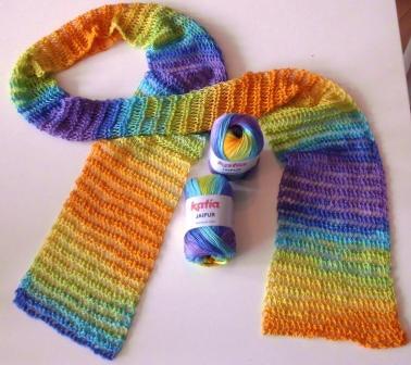 Schmaler gestrickter Schal mit Regenbogen-Farbverlauf und zwei Knäueln Verlaufsgarn auf hellem Untergrund