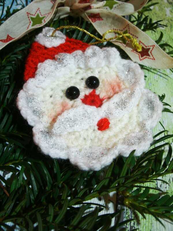 Gehäkelter Weihnachtsmannkopf mit Glitzer, roter Mütze und Sternband auf Tannenzweigen
