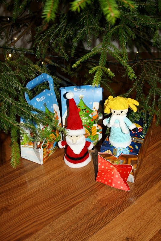 Gehäkelter Weihnachtsmann und gehäkelte Puppe vor Geschenktüten und Tannenbaum