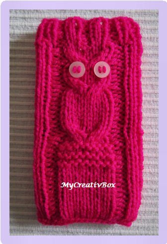 Gestricktes Etui in Fuchsia mit Eulenmotiv und zwei runden, hellen Knöpfen als Augen, auf hellem Hintergrund liegend.