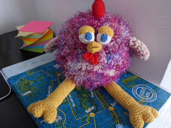 Gehäkeltes Amigurumi-Huhn, pink-lila, mit gelbem Schnabel und Füßen sowie rotem Kamm