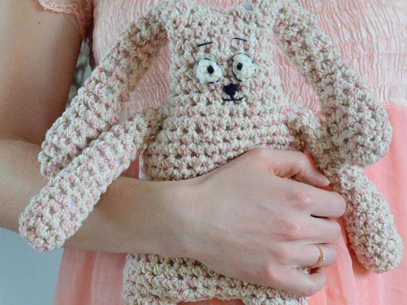 Hand hält einen gehäkelten Hasen in Rosa und Creme mit großen Augen und langen Ohren.
