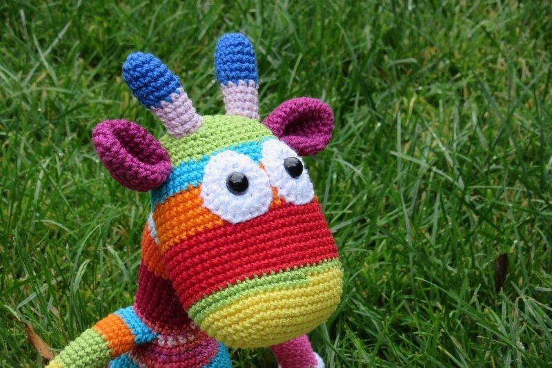 Bunte gehäkelte Amigurumi-Giraffe mit Streifen auf Gras