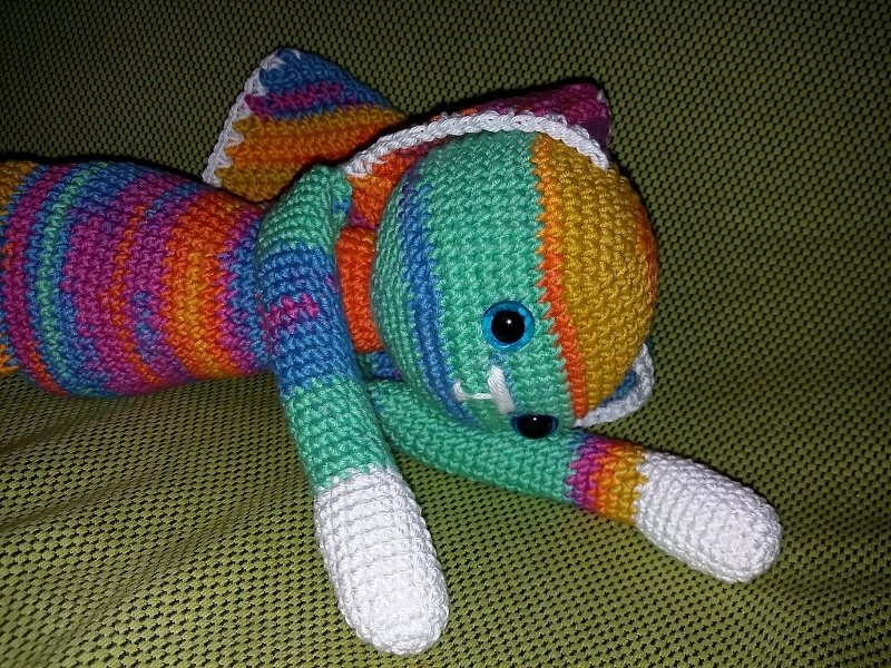 Gehäkelter gestreifter Amigurumi-Hase liegend, mehrfarbiges Garn mit weißen Pfoten