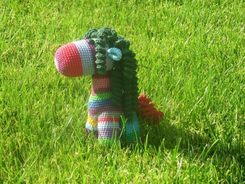 Gehäkeltes, bunt gestreiftes Amigurumi‑Zebra mit grüner Mähne auf Gras.