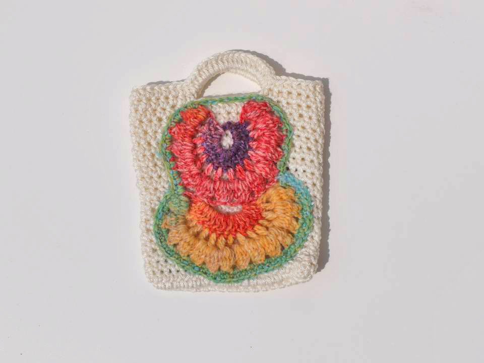 Mini-Tasche gehäkelt mit bunten Blütenapplikationen auf cremefarbenem Untergrund