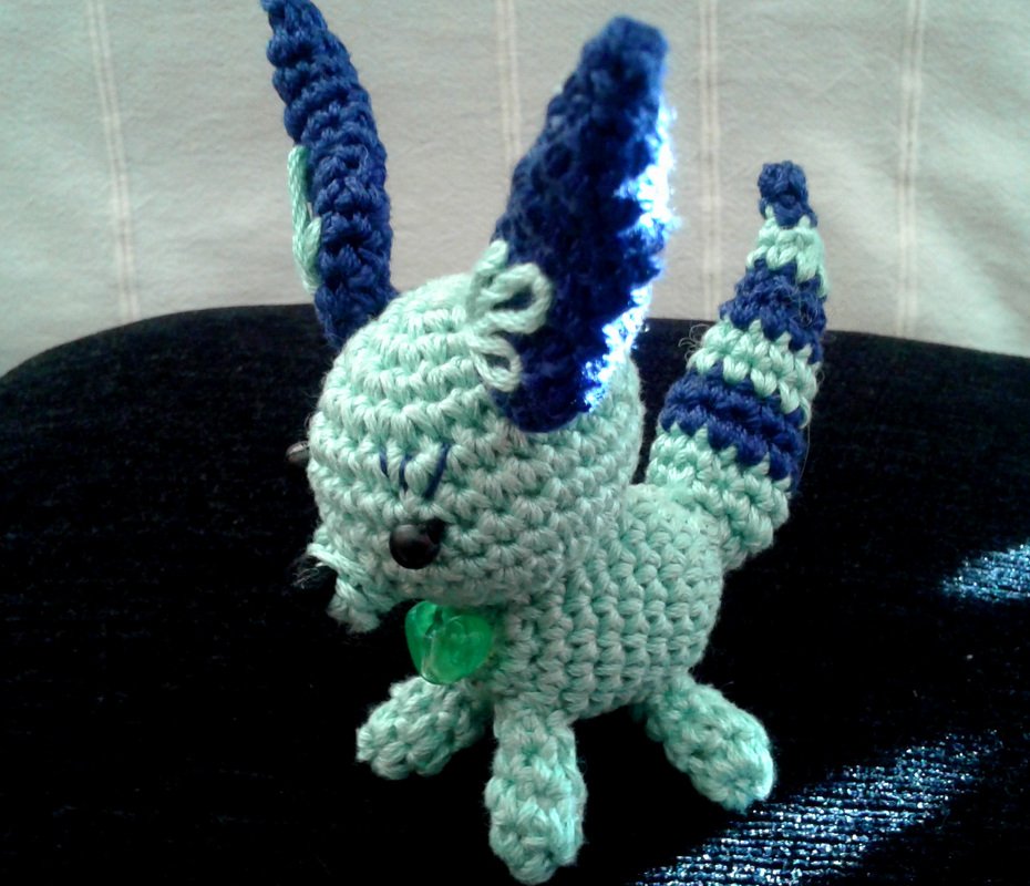 Kleines gehäkeltes Amigurumi-Tier in Mintgrün und Blau mit gestreiftem Schwanz und Herz