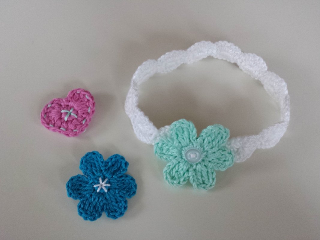 Weißes gehäkeltes Babystirnband mit mintgrüner Blüte und zwei separaten Häkelapplikationen (rosa Herz, blaue Blume)