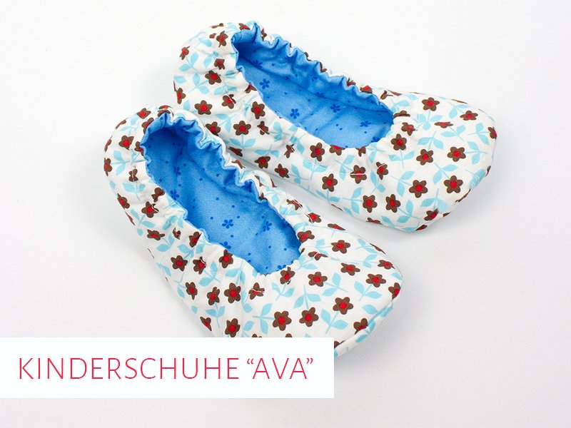 Paar genähter Kinderschuh-Ballerinas mit weißem Stoff und roten Blumenmuster, blaues Innenfutter