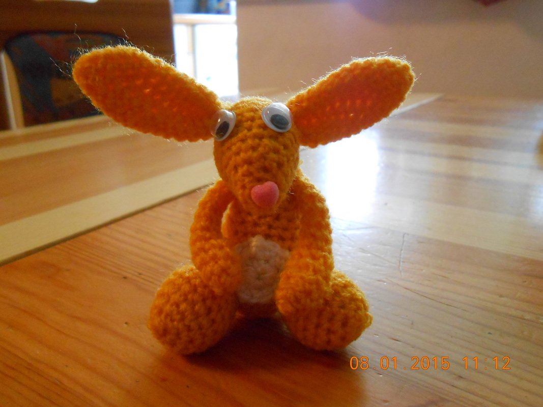 Orangener gehäkelter Amigurumi-Hase mit langen Ohren, weißem Bauch, rosa Herznase und Wackelaugen