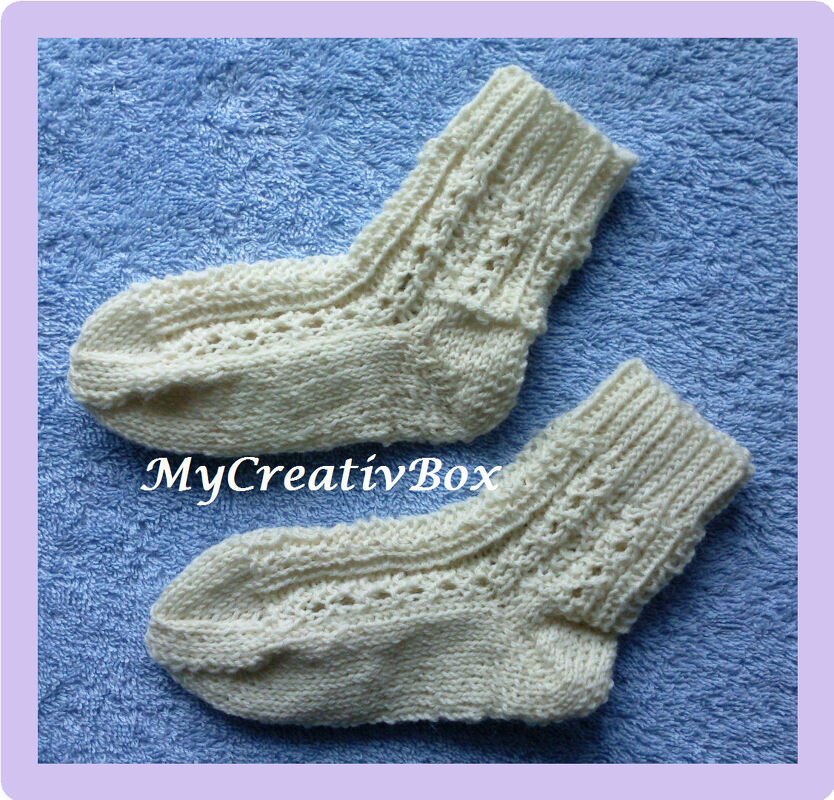 Cremefarbene gestrickte Babysocken mit Lochmuster auf blauem Untergrund