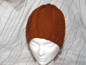 Rostbraune gestrickte Mütze mit Zopfmuster auf weißem Mannequinkopf
