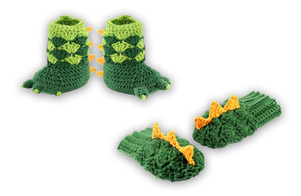 Gehäkelte grüne Dinosaurier-Babyschuhe und Fäustlinge mit orangen Stacheln auf weißem Hintergrund