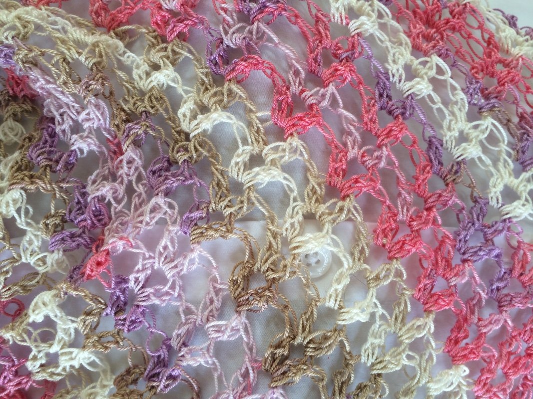 Detaillierte Ansicht eines gehäkelten Netzmusters in Rosa, Lila, Beige und Cremeweiß auf hellem Untergrund.