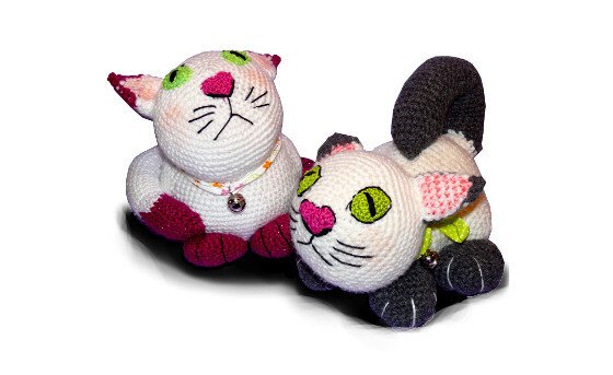 Zwei weiße Amigurumi-Katzen mit magenta- und grauen Akzenten und kleinen Glöckchen