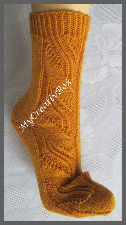 Senfgelbe gestrickte Socke mit Zopf- und Blattmuster auf hellem Untergrund