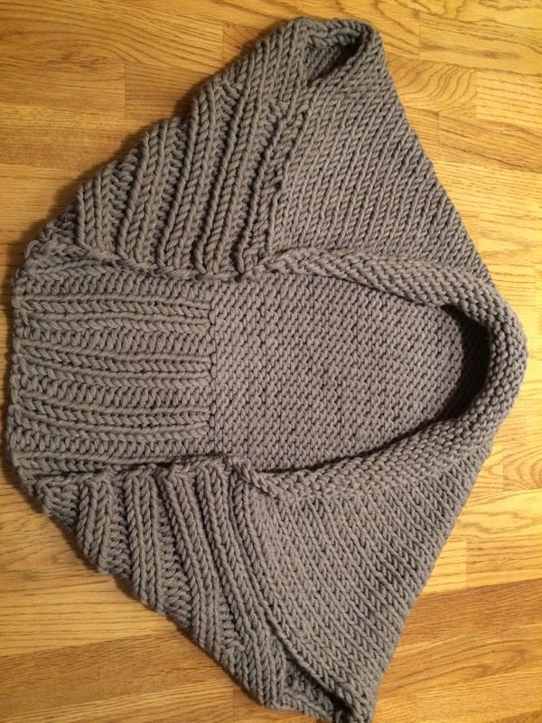 Grau gestrickter Kapuzenponcho für Kinder liegend auf Holzfußboden