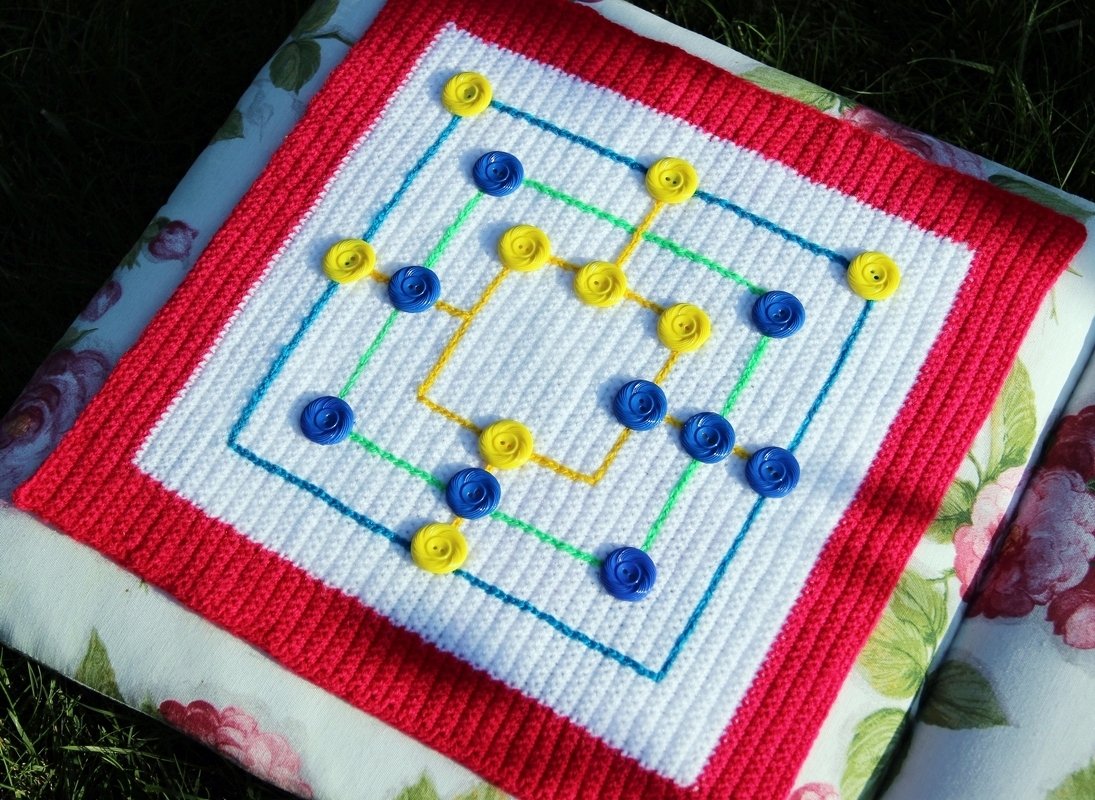 Quadratisches gehäkeltes Spielbrett weiß mit rotem Rand und aufgenähten gelben und blauen Markern