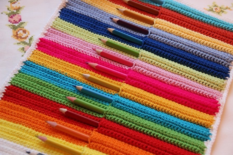 Nahaufnahme einer gehäkelten Stifterolle mit bunten Taschen und Farbstiften