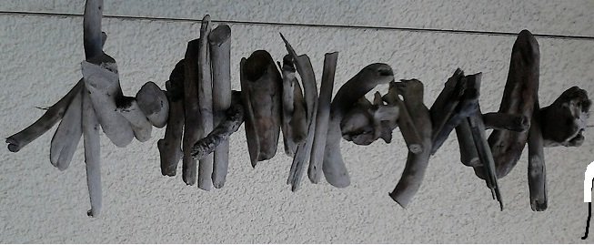 Horizontale Girlande aus Treibholzstücken an einer Schnur vor heller Wand