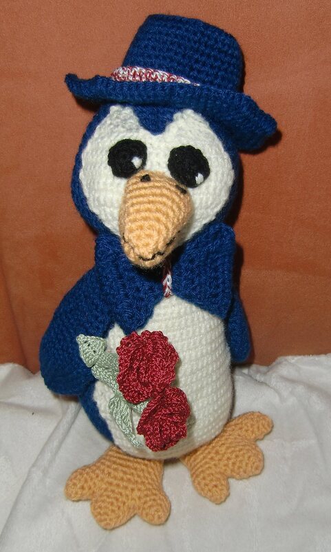 Gehäkelter blauer Amigurumi-Pinguin mit Hut, Schal und roten Rosen