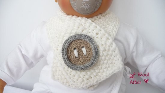 Cremeweißer gehäkelter Babyschal mit großem runden Zierknopf in Braun und Grau, an einem Baby getragen.