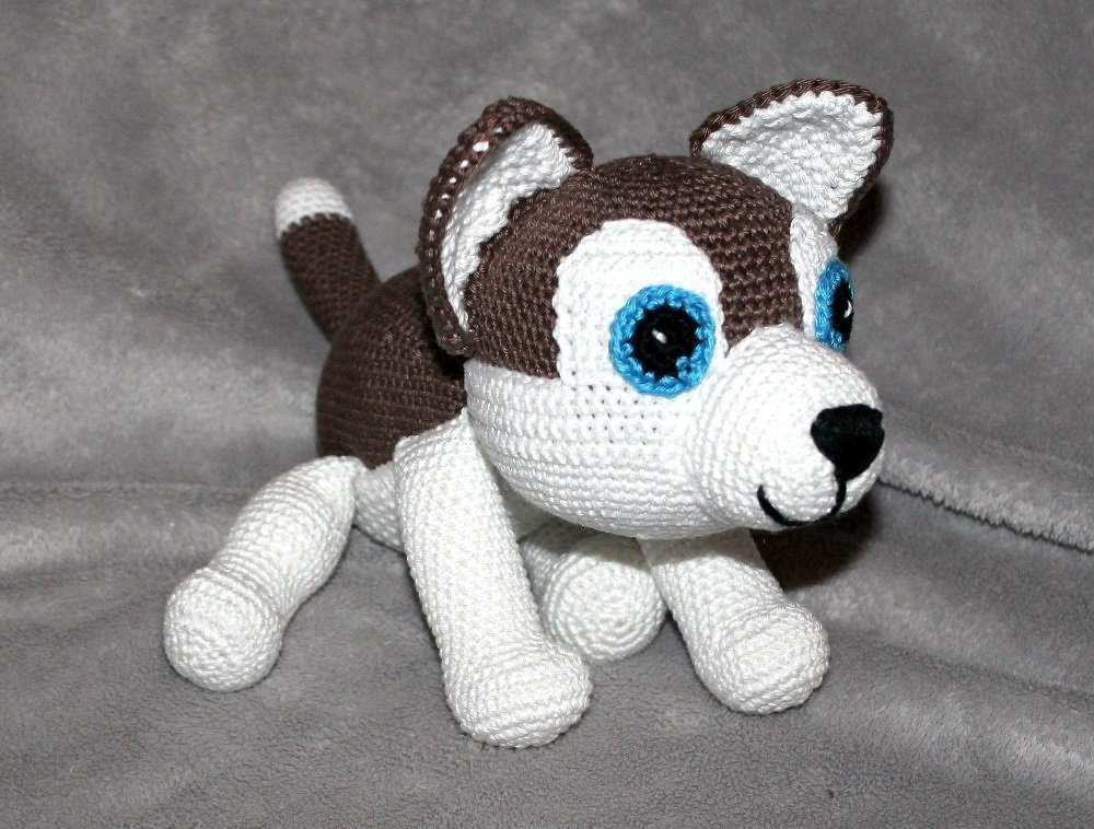 Gehäkeltes Husky-Amigurumi in Braun und Weiß mit blauen Augen auf grauem Hintergrund