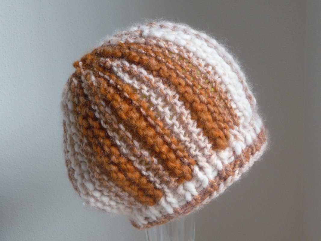 Gestrickte Mütze in Braun-, Beige- und Weißtönen mit Rippen- und Streifenstruktur.