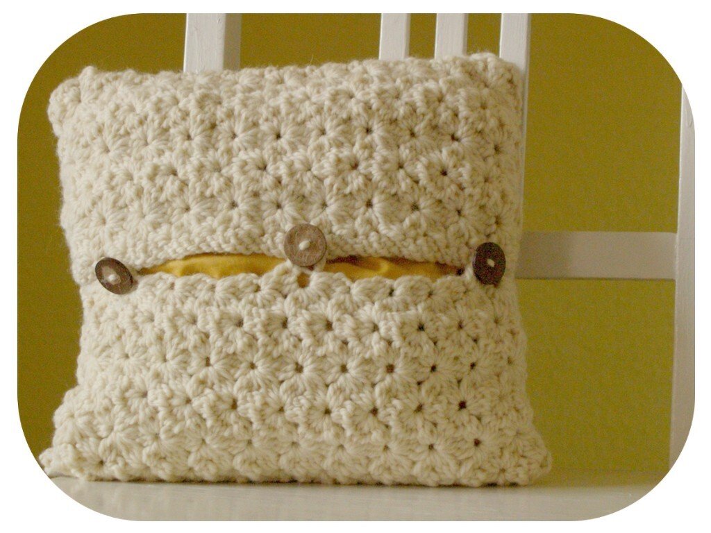 Gehäkelter Kissenbezug in Creme mit Knopfleiste und gelbem Innenkissen auf weißem Stuhl vor grünem Hintergrund