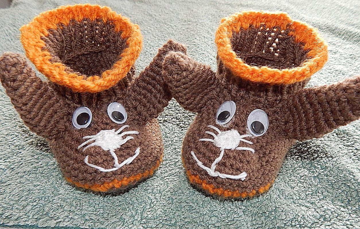 Braun-orange gehäkelte Babyschuhe im Tierdesign mit Wackelaugen auf hellem Untergrund