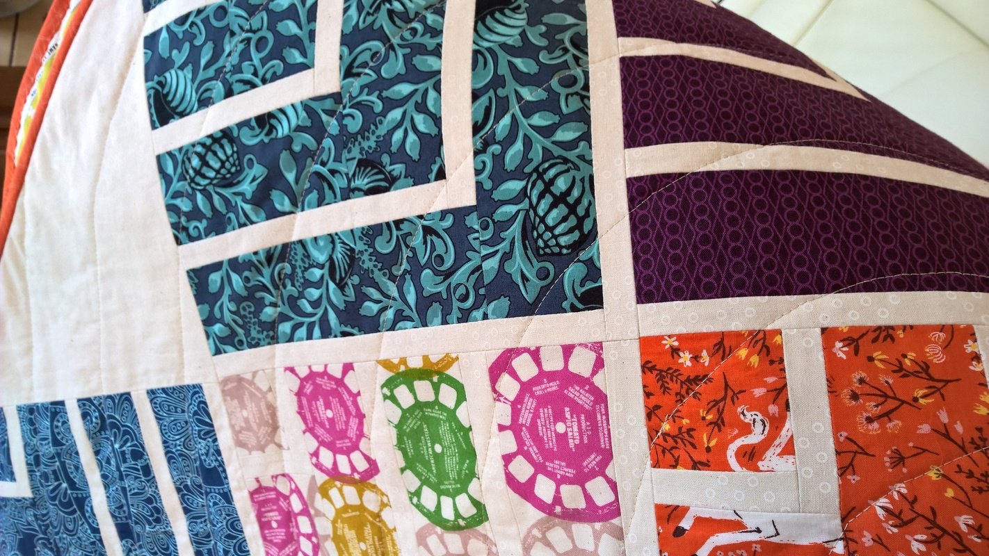 Nahaufnahme einer Patchwork-Decke mit bunten Quadraten und hellen Sashingstreifen