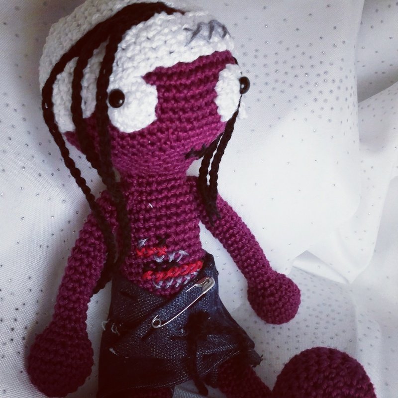 Violette Amigurumi-Häkelpuppe mit weißem Kopf, schwarzen Haarsträhnen und Jeansrock mit Sicherheitsnadel