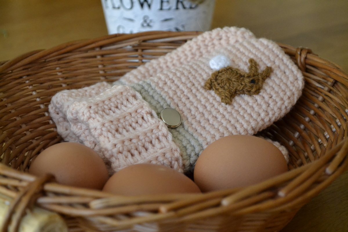 Kleiner rosafarbener gehäkelter Osterbeutel mit Hasenmotiv und Druckknopf im Weidenkorb mit Eiern