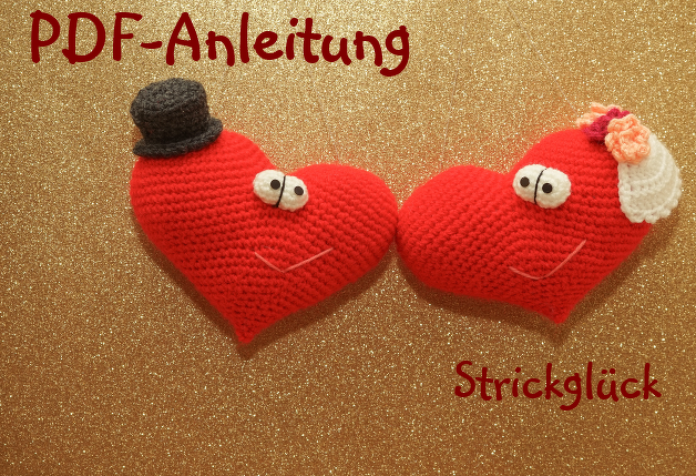 Zwei rote Amigurumi-Herzen, eines mit Zylinder, das andere mit Schleier und Blüten, vor goldenem Glitzerhintergrund; Schriftzug ‚PDF-Anleitung‘