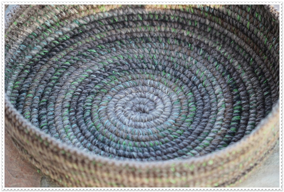 Top-down close-up of a round crocheted basket in grey-brown yarn with green flecks