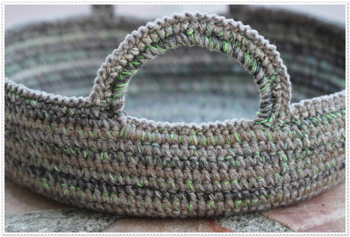 Round crocheted basket with two handles, variegated grey-brown yarn with green flecks.