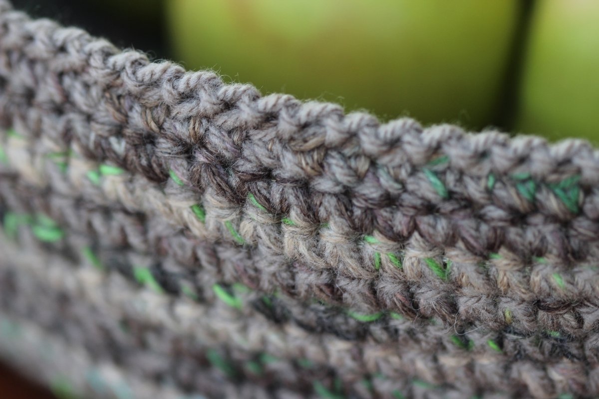 Close-up of dense crochet stitchwork on a basket edge showing rolled rim and speckled yarn
