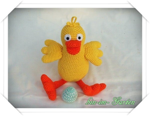 Gehäkeltes gelbes Küken-Amigurumi mit orangefarbenem Schnabel und Beinen, neben einem hellblauen Häkel-Ei
