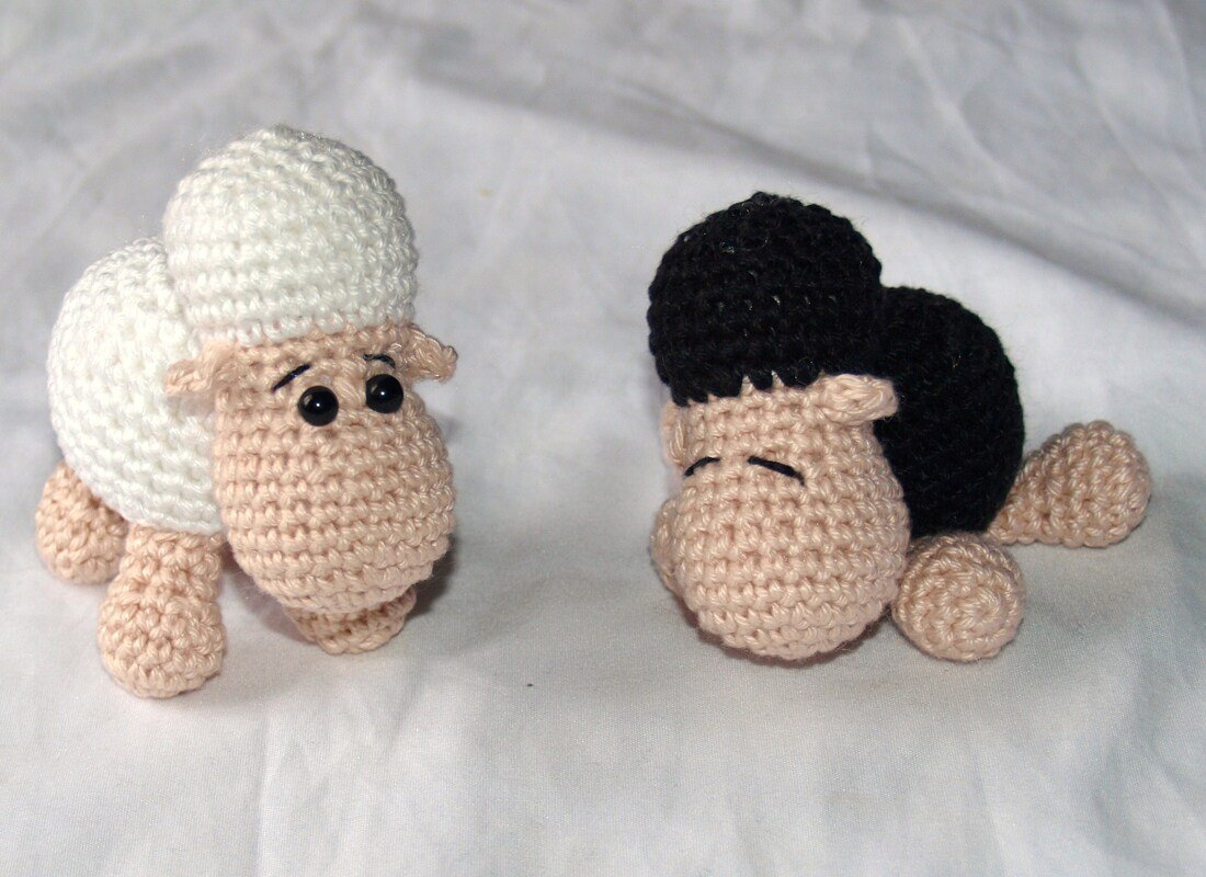 Zwei gehäkelte Amigurumi-Schafe, ein weißes stehend und ein schwarzes liegend