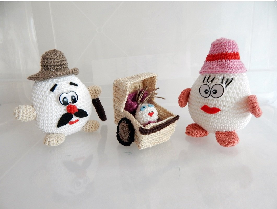 Zwei gehäkelte Amigurumi-Eier mit Hüten und ein kleiner gehäkelter Wagen mit Baby-Ei