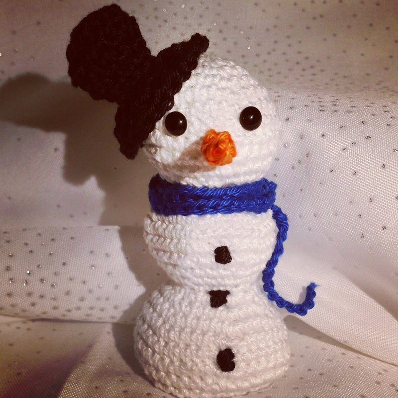 Weißer gehäkelter Amigurumi‑Schneemann mit schwarzem Hut und blauem Schal