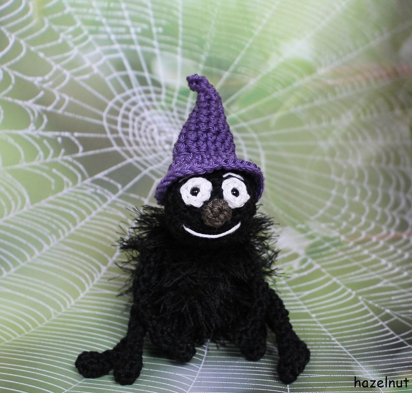 Schwarze Amigurumi-Spinne mit lila Hexenhut vor Spinnennetz
