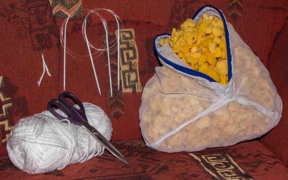 Stricknadeln, Wolle, Schere und Beutel mit Schaumstoffflocken auf rotem, gemustertem Stoff