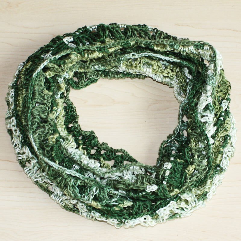 Gehäkelter Loop-Schal in grünen Farbabstufungen auf hellem Holzuntergrund
