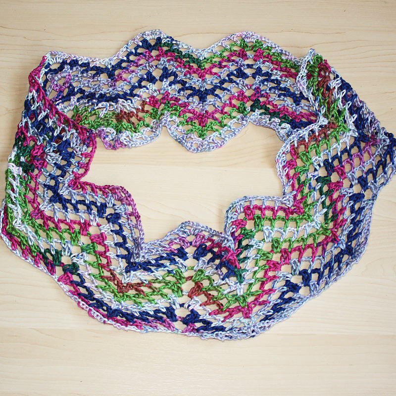 Mehrfarbiger gehäkelter Loop mit Wellen- und Muschelrand, auf hellem Holz.