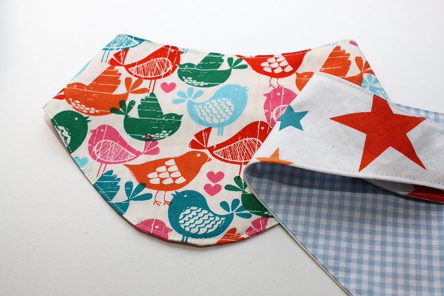 Wendbares Babybandana mit Vogelprint auf der einen Seite und roten Sternen auf der anderen, sichtbare Nahtkante