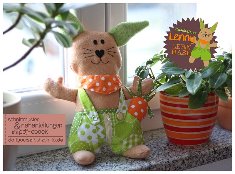 DIY-Stoffhase mit grüner Latzhose, sichtbarem Reißverschluss, Knöpfen und orange gepunktetem Halstuch auf einer Fensterbank