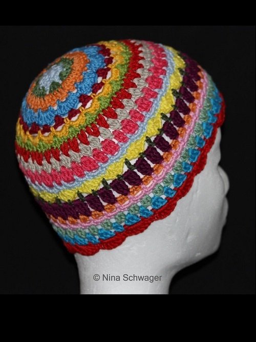 Gehäkelte Mütze in leuchtenden Regenbogenfarben auf weißem Kopfmodell, seitliche Ansicht