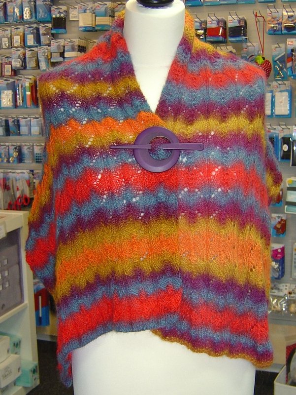 Bunt gestreifter Strickschal mit Lochmuster und lila Tuchnadel auf Schneiderpuppe